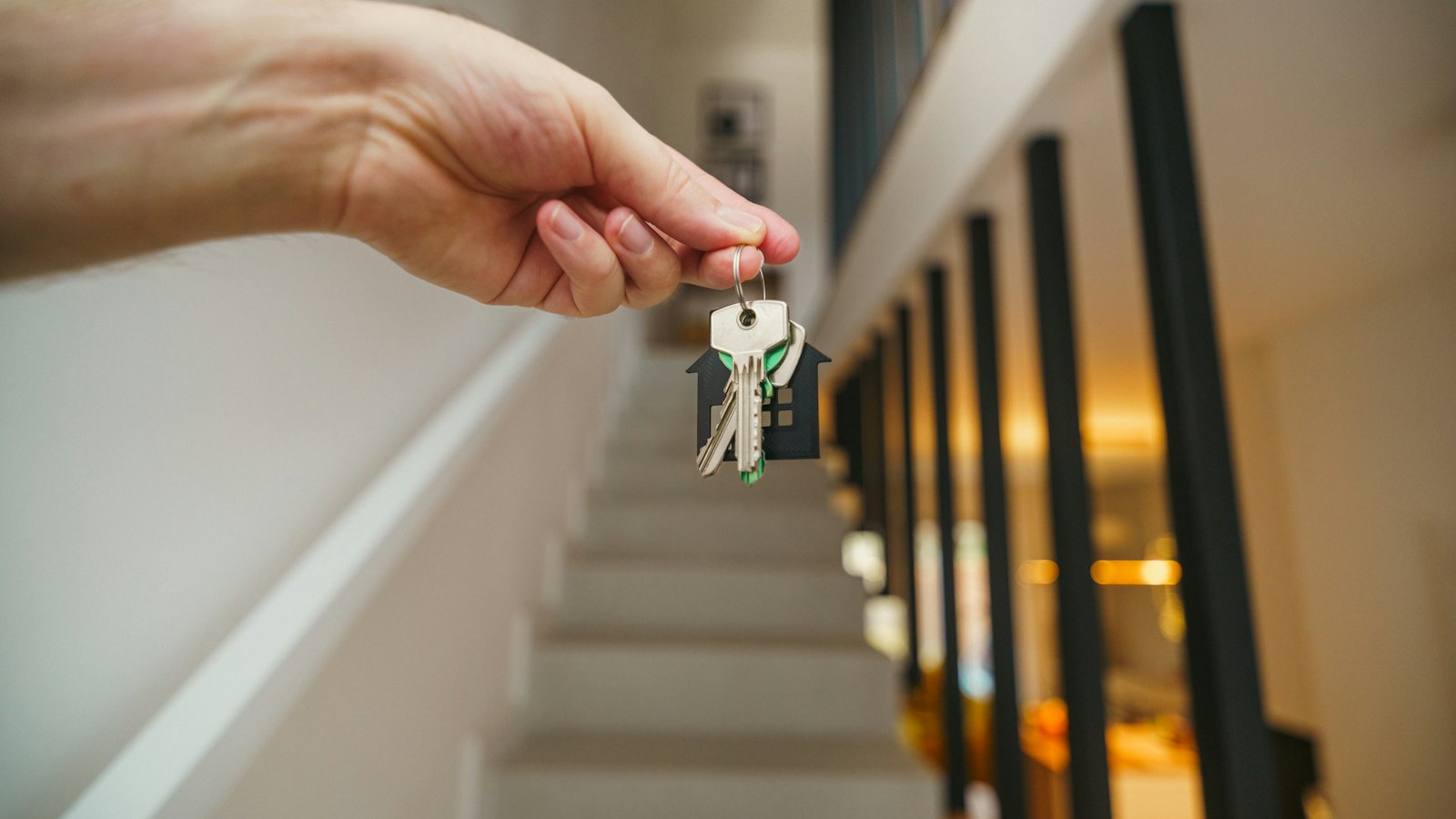 Main tenant un trousseau de clés avec un porte-clés en forme de maison